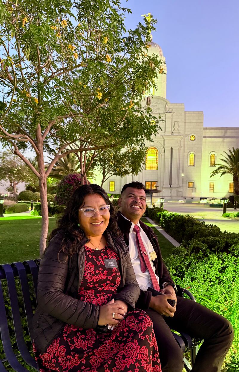 Um homem e uma mulher usando crachás de missionários estão sentados sorrindo em frente ao Templo de Arequipa Peru na primeira semana de agosto de 2025.