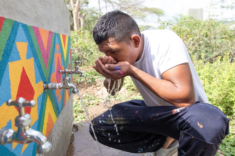 Keiber Epinayu, um jovem artista e líder comunitário Wayúu, bebe água de uma torneira nova após pintar a infraestrutura em La Guajira, Colômbia, em fevereiro de 2024.