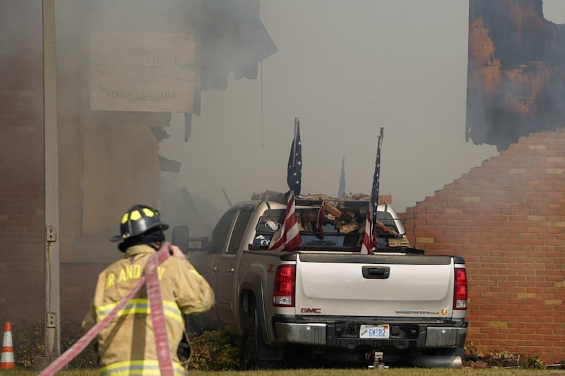 Um veículo que foi arremessado contra o prédio do Grand Blanc Ward está envolvido em fumaça enquanto um bombeiro trabalha no local em Grand Blanc, Michigan, domingo, 28 de setembro de 2025.