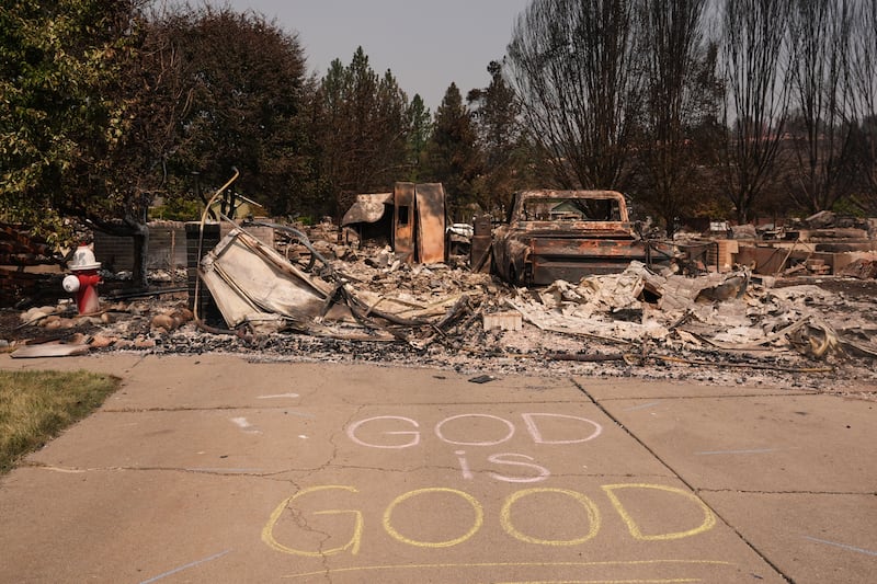Um sinal "God is good" está escrito em giz ao lado de uma boca de incêndio e uma casa queimada após um incêndio florestal atingir a parte noroeste de Spokane, Washington, terça-feira, 4 de agosto de 2026.