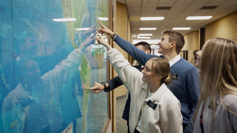 Missionários apontam para sua missão designada em um mapa mundial durante a gravação de um novo vídeo no Centro de Treinamento Missionário de Provo.