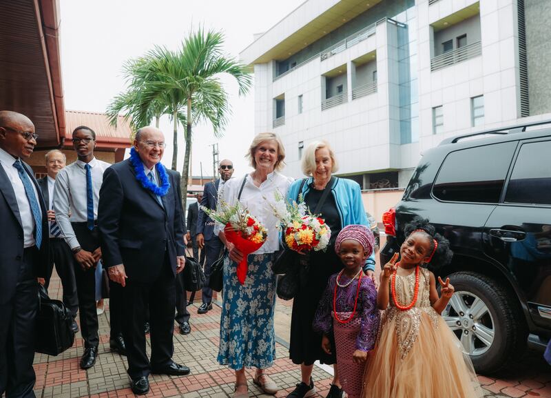 Elder Quentin L. Cook, Sister Mary Cook, Sister Rosalie Ringwood e outros são cumprimentados por duas menininhas nigerianas na sua chegada ao Lagos Nigeria Ikeja Stake Center em 14 de fevereiro de 2026.
