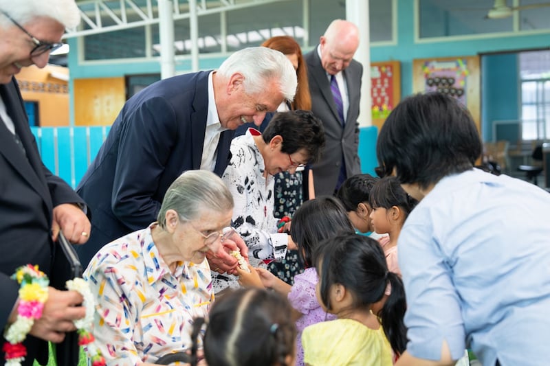 Élder Dieter F. Uchtdorf e Irmã Harriet Uchtdorf se juntam à Irmã Louise Horgan para cumprimentar crianças na Good Shepherd Sisters Bangkok.