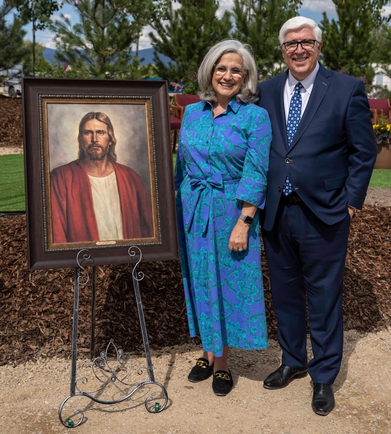 Elder José A. Teixeira e Sister Filomena Teixeira, posam para uma foto ao lado de uma pintura do Salvador na cerimônia de abertura de terra do Templo de Missoula Montana.