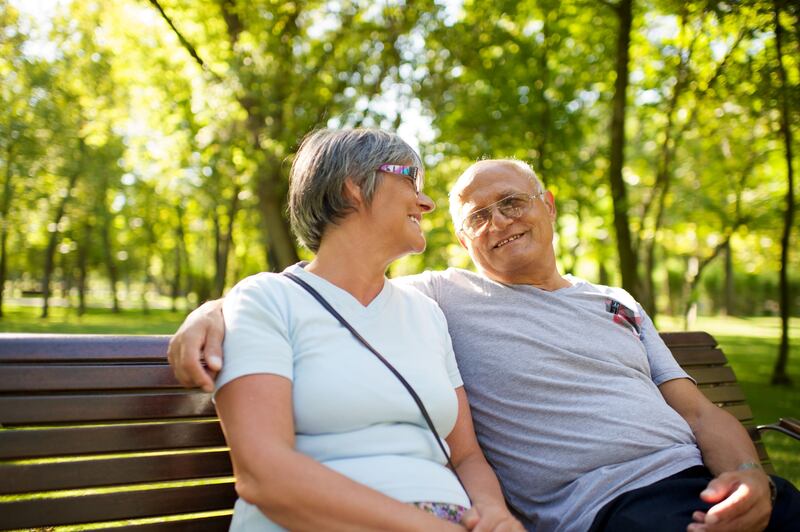 An elderly couple smiles together on a park bench.