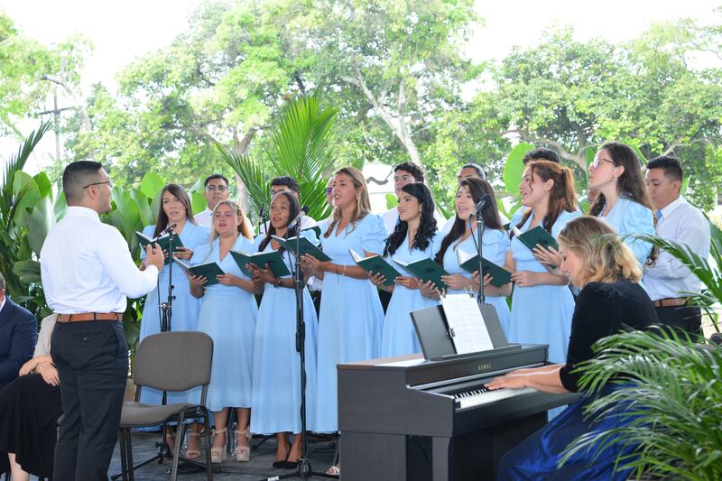 Um coro de mulheres com vestidos azul claro cantando ao ar livre.