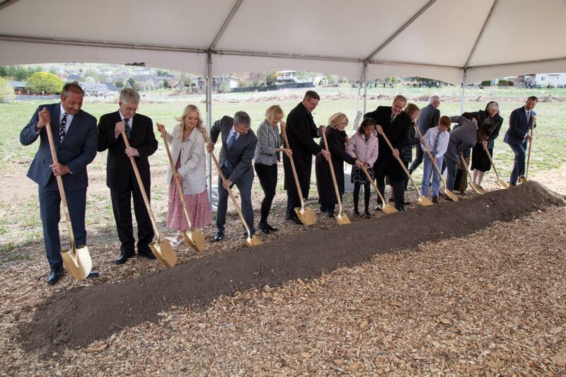 Um grupo de convidados revolve a terra com pás na abertura de terra do Templo de Lindon Utah, em 23 de abril de 2022. Élder Kevin W. Pearson, Setenta Autoridade Geral e presidente da Área Utah, e sua esposa, a irmã June Pearson, estão no centro.