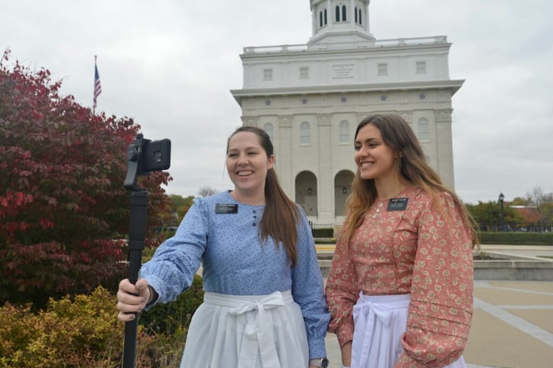 Sister Karly Robison e Sister Meg Taylor, missionárias que servem nos Sítios Históricos de Illinois, oferecem um tour virtual em frente ao Templo de Nauvoo Illinois em 2020.