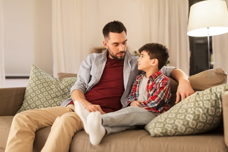 Um pai e um filho conversam sentados em um sofá.