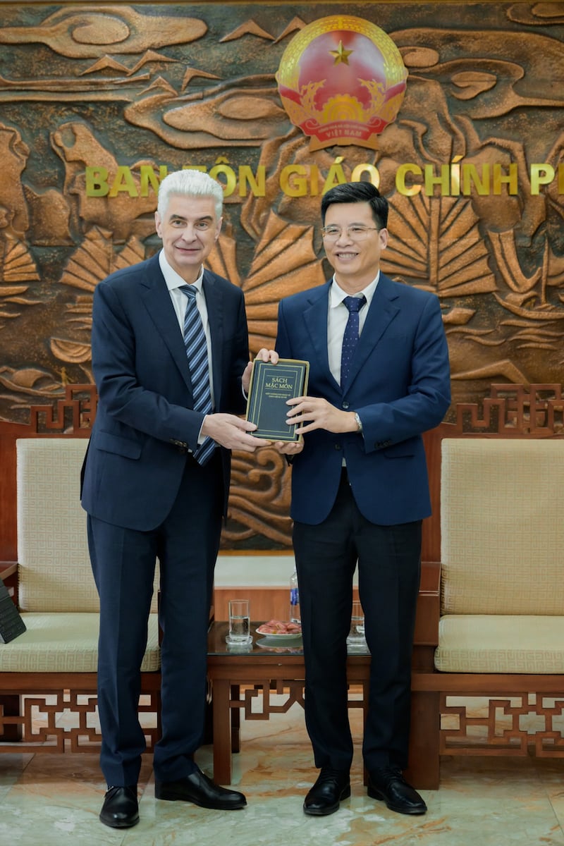 Elder Gérald Caussé do Quórum dos Doze Apóstolos entrega o Livro de Mórmon em vietnamita ao Vice-Presidente do Comitê Governamental para Assuntos Religiosos, Nguyễn Tiến Trọng, em uma reunião nos escritórios do Comitê em Hanói, Vietnã, em 23 de abril de 2026.