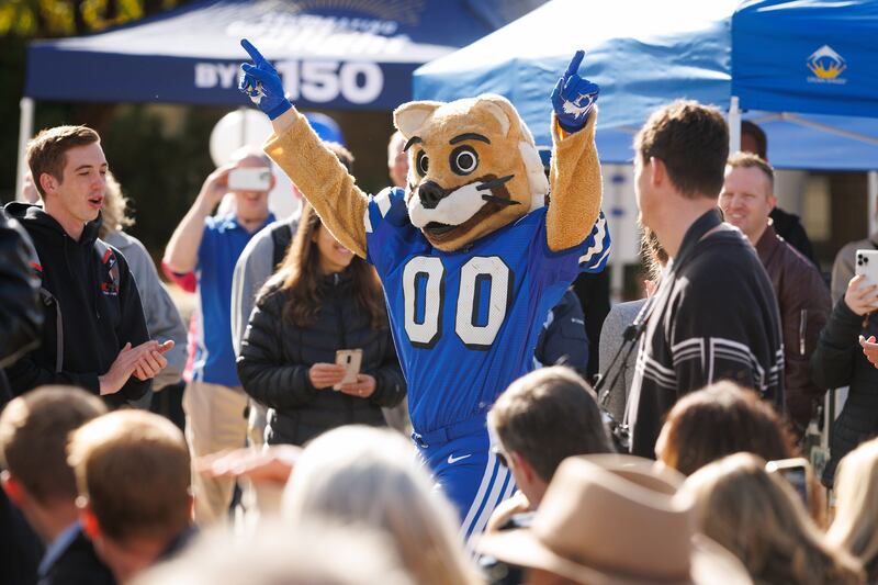 Durante um evento do Dia do Fundador em 16 de outubro de 2025, o mascote Cosmo da BYU faz uma aparição vestindo sua fantasia dos anos 1970 enquanto líderes da universidade abrem uma cápsula do tempo das celebrações do centenário da universidade de 1975.