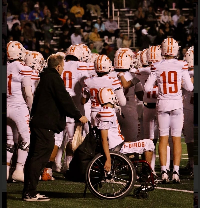 O pai Ken Cooper empurra seu filho, Matthew Cooper, em sua cadeira de rodas à beira do campo durante um jogo de futebol americano da Timpview High School em Provo, Utah, no outono de 2024.