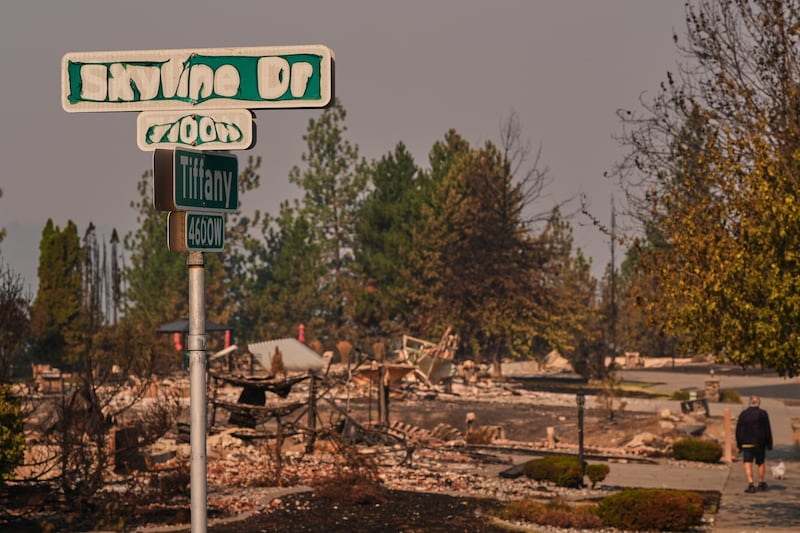 Uma placa de rua mostra sinais de danos causados pelo fogo enquanto uma pessoa passeia com seu cachorro após um incêndio florestal atingir a parte norte de Spokane, Washington, segunda-feira, 3 de agosto de 2026.