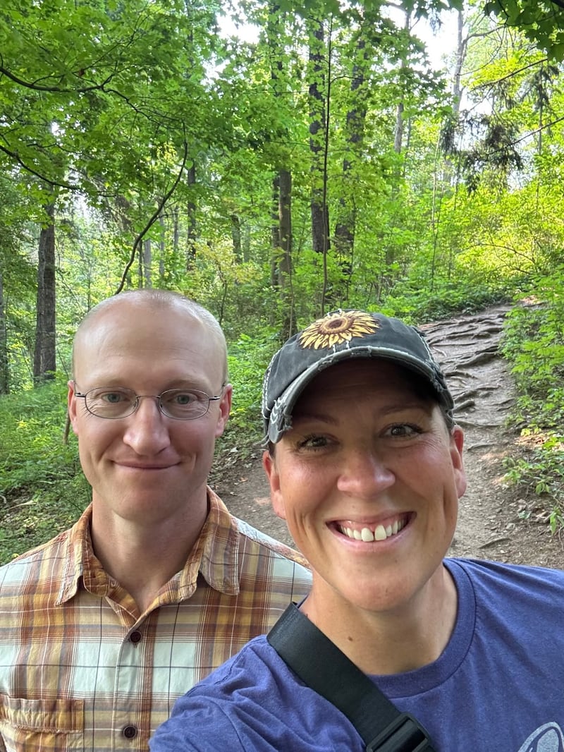Glenn e Erica Nielson estão de pé juntos em frente a uma trilha de terra.