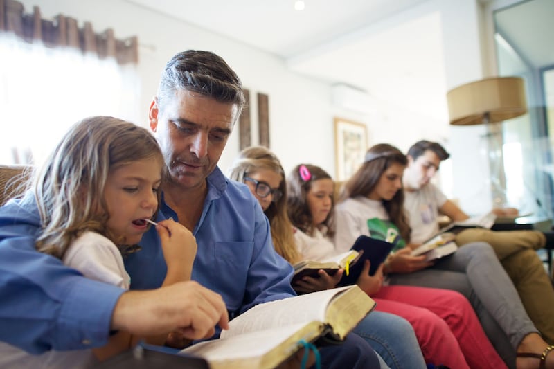 Um pai se senta com seus filhos em sua sala de estar para ler juntos as escrituras em Portugal.