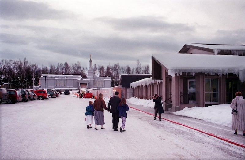 Com o Templo de Anchorage, Alasca ao fundo e o salão de reuniões adjacente à direita, uma família é fotografada chegando para a dedicação do templo em 9 de janeiro de 1999, em Anchorage, Alasca.