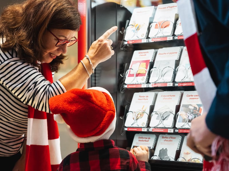 Uma família olha para cartões de doação em uma Light the World Giving Machine em Montreal, Québec, Canadá, em dezembro de 2025.
