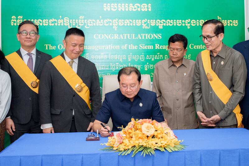 Chheang Ra, ministro da saúde do Camboja, ao centro, com Elder Benjamin M.Z. Tai, Setenta Autoridade Geral e presidente da Área Ásia, centro-esquerda, assina livro comemorativo na cerimônia de celebração do novo centro cardíaco.