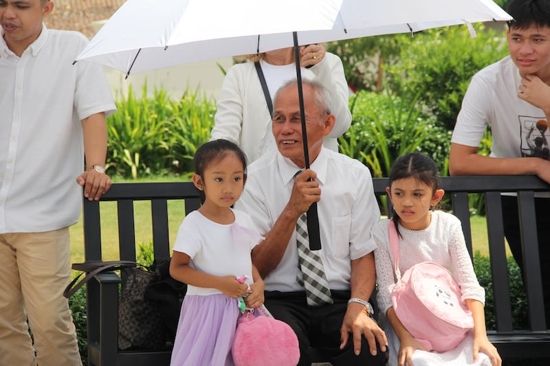 Um avô senta-se sob um guarda-sol com duas meninas nos jardins do Templo de Davao Filipinas no último dia da casa aberta ao público, 10 de abril de 2026.