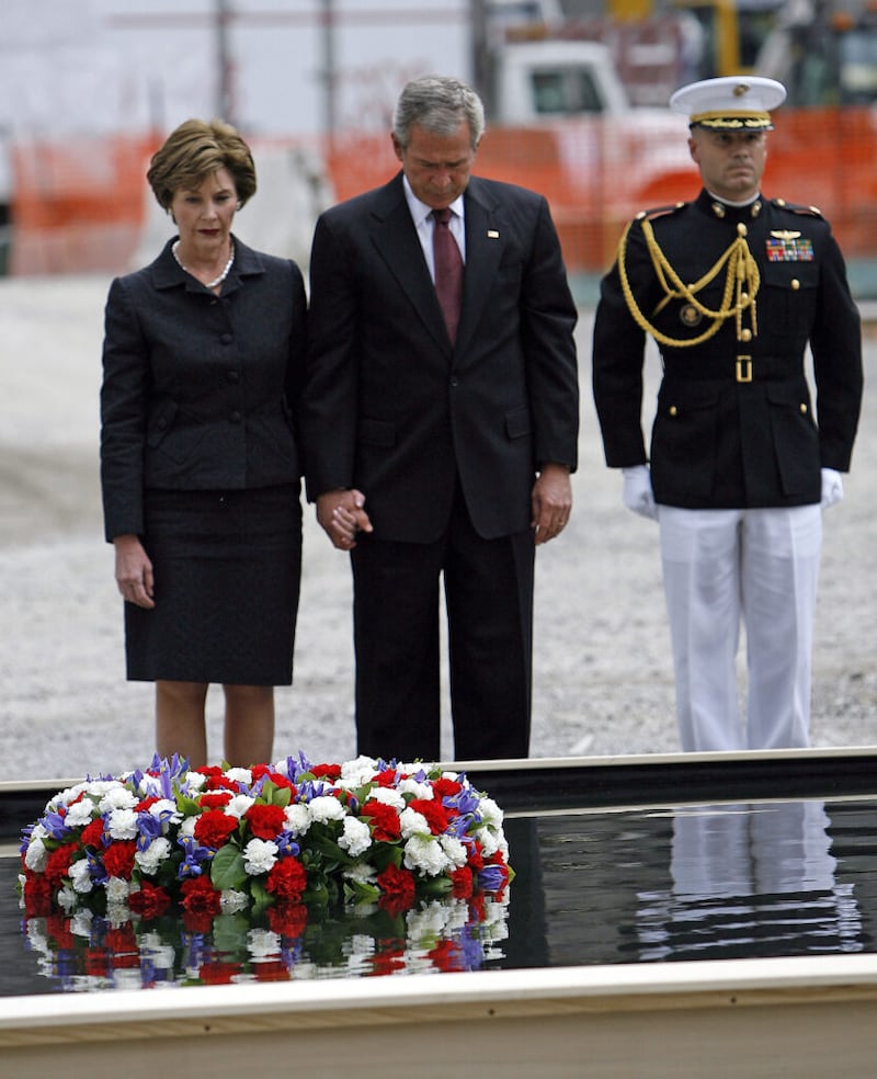 Uma escolta militar está atenta enquanto o presidente Bush e a primeira-dama Laura Bush fazem um momento de silêncio depois de colocar uma coroa de flores em um espelho d’água no marco zero no domingo, 10 de setembro de 2006. Bush estava em Nova York para homenagear o quinto aniversário dos ataques terroristas de 11 de setembro de 2001. (AP Photo/Jason DeCrow).