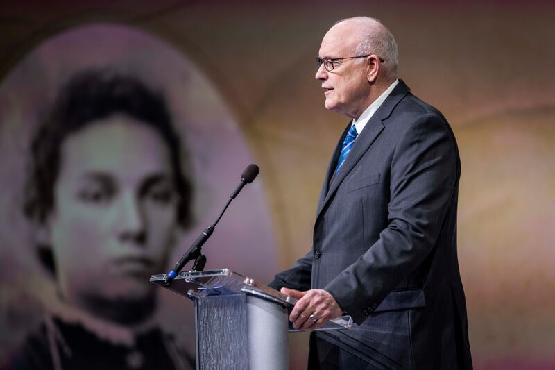 Élder Paul V. Johnson, da Presidência dos Setenta, fala durante um devocional no campus da BYU em 14 de março de 2023. Na tela do projetor há uma foto de sua avó, Amalie Hollenweger Amacher.