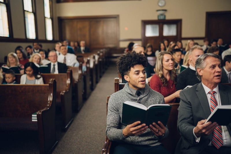 As pessoas se sentam em bancos da igreja e cantam como congregação.