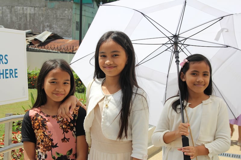Três meninas sorriem para uma foto fora do Templo das Filipinas Davao no último dia da casa aberta ao público, 10 de abril de 2026.