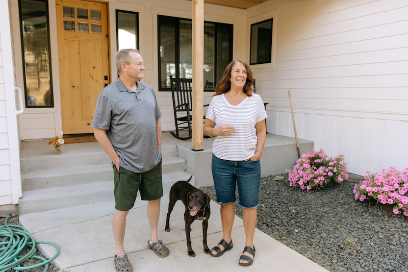 Em pé do lado de fora com sua cachorra Mia, Todd e Debbie Rogers contam a história de sua casa ter sobrevivido aos incêndios florestais de Spokane em Spokane, Washington, no sábado, 22 de agosto de 2026.